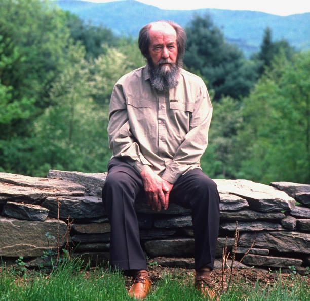 Nobel prize-winning author and critic of Soviet regimes Aleksandr Solzhenitsyn sitting on low stone wall outside his home.
