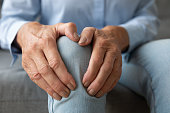 Old woman touching knee feeling pain suffering from osteoarthritis, closeup