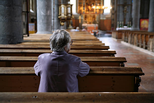 older woman praying in an almost empty church, rear view - an old woman praying at the church stock pictures, royalty-free photos & images