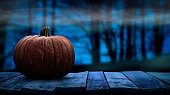 One spooky halloween pumpkin blank template on a wooden bench with a misty forest night background.