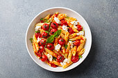 Pasta penne with roasted tomato, sauce, mozzarella cheese. Grey stone background. Top view.