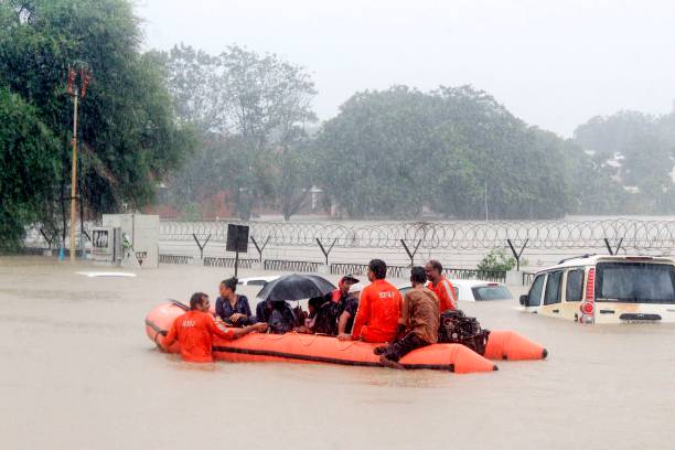 People are being rescued on a boat by personnel from the National Disaster Response Force as they pass by vehicles submerged floodwaters of Vadodara,...