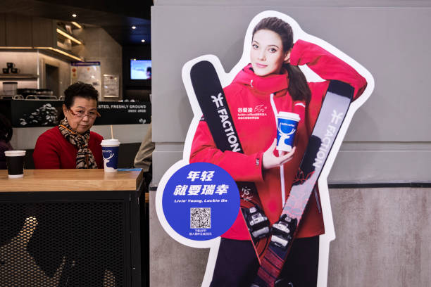 People drink coffee near a model of freestyle skiing gold medalist Eileen Gu, who competes for China, at Luckin Coffee on February 9, 2022 in Wuhan,...