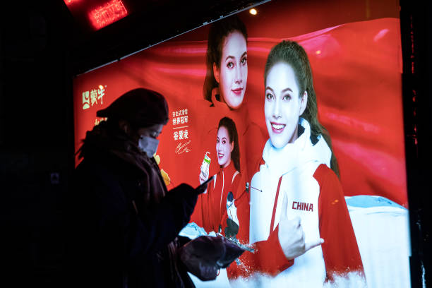 People walk in front of a bus stop billboard of freestyle skiing gold medalist Eileen Gu who competes for China, in as street on February 9, 2022 in...