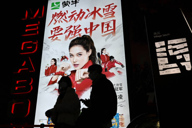 People walk in front of an advertising billboard showing China's US-born gold medallist Gu Ailing Eileen at a shopping mall in Beijing on February 9,...