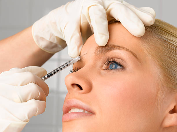 person injecting young woman's forehead with small syringe, close up, side view, studio shot - injeção no rosto - fotografias e filmes do acervo