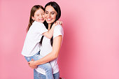 Photo of beautiful young mother hold arms little daughter two ladies hugging best friends lovely feelings eyes closed wear casual t-shirts jeans isolated pastel pink color background