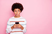 Photo of pretty dark skin lady holding telephone doubtful about new instagram post wear white striped pullover isolated pastel pink color background
