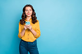 Photo of pretty wavy lady holding telephone hands thinking over creative post text idea looking side empty space wear yellow shirt trousers isolated blue color background