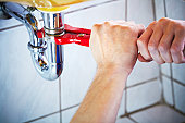 Plumber hands holding wrench and fixing a sink in bathroom