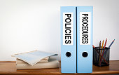 Policies and Procedures binders in the office. Stationery on a wooden shelf