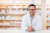 Portrait of a cheerful young pharmacist leaning on a counter at drugstore, looking at camera.