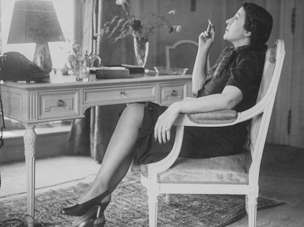 Portrait of Greek actress Katina Paxinou smoking a cigarette as she sits at a desk, during a trip to England following the occupation of her home...