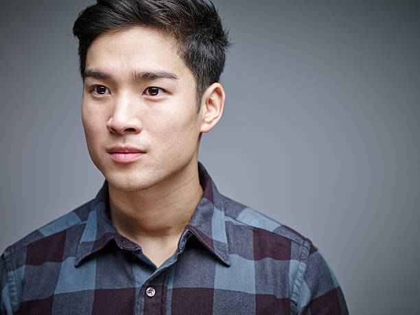 portrait of seriuos looking young man in front of grey background - serious asian man stock pictures, royalty-free photos & images