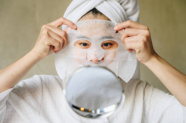 portrait of young woman looking her face in mirror before applying facial mask for enhance her skin. - face mask skincare stock pictures, royalty-free photos & images