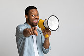 Positive african guy shouting in megaphone over grey background