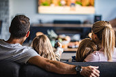 Rear view of a family watching TV on sofa at home.