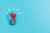 Red heart in light bulb on blue background with copy space.