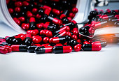 Red-black antibiotic capsule pills spill out of white plastic bottle container and drug tray. Pharmaceutical industry. Prescription drug. Global healthcare. Antimicrobial drug resistance. Pharmacy.