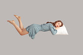 Relaxed girl in vintage ruffle dress levitating in mid-air, sleeping on stomach lying comfortable cozy on pillow