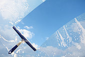 Rubber squeegee cleans a soaped window and clears a stripe of blue sky with clouds, concept for tranparency or spring cleaning, copy space in the background