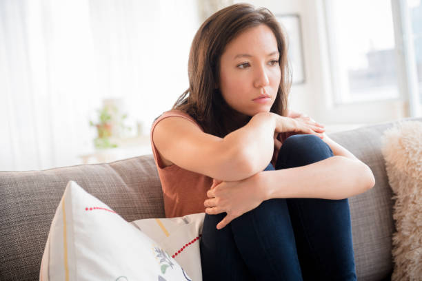 sad mixed race woman sitting on sofa - sad asian woman stock pictures, royalty-free photos & images
