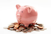 Save money, financial planning of personal finances and being thrifty concept theme with a pink piggy bank sitting on a pile of bronze and silver colored coins isolated on white background