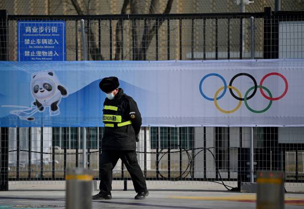 Security personnel walk in front of a picture of Bing Dwen Dwen, a mascot of the 2022 Beijing Winter Olympic Games and the Olympic Rings, at the...