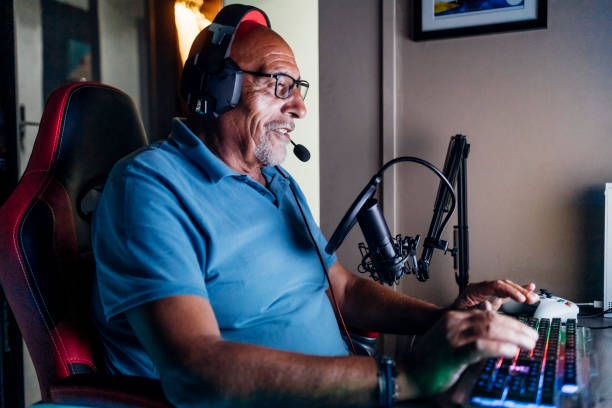 senior man doing online streaming while playing video game at home - streaming de videogames - fotografias e filmes do acervo
