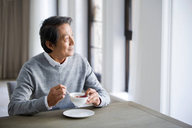 senior man eating nutritious porridge - asian old rich man stock pictures, royalty-free photos & images