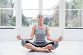 Senior woman sitting cross legged doing yoga at home