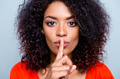 Shh! Closeup portrait of mysterious charming woman with modern hairdo asking for keeping silence holding forefinger on plump lips isolated on grey background
