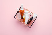 Shopping basket full of cosmetic bottles and packaging on pink background, view from above. Cosmetics sale or discount concept.