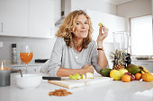 Shot of a woman preparing and eating fruit before making a smoothie