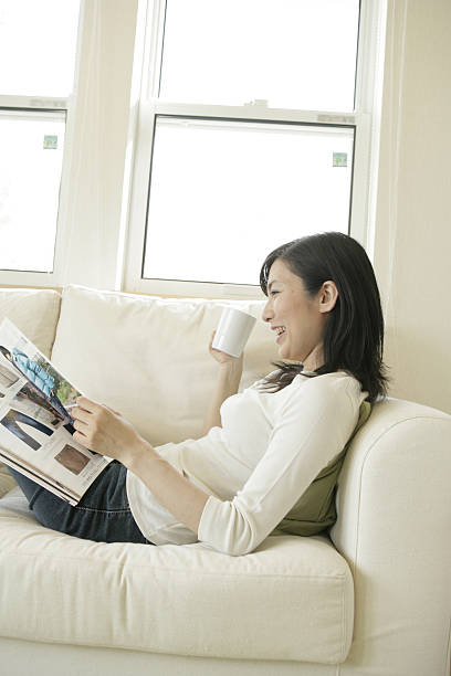 Side profile of a mid adult woman holding a magazine and a coffee cup