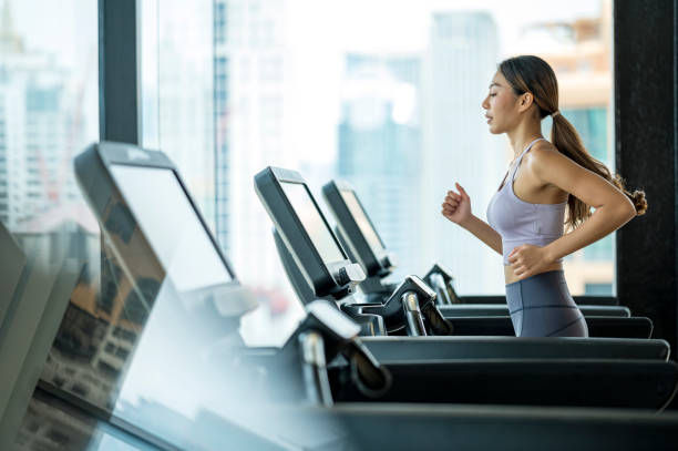 side view of young asian women athlete running or jogging on treadmill in a hotel sport club. -  gym stock pictures, royalty-free photos & images