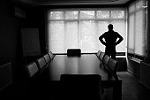 Silhouette Of Lonely Businessman Standing By Boardroom Table In Office