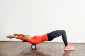 Slim woman in sport tight pants doing exercise with foam roller massager on floor, relaxing and stretching spine muscles