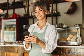 Small business owner holding a smartphone in her cafe