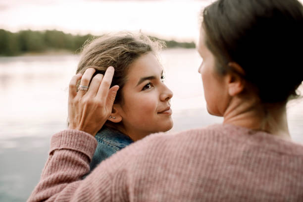 smiling daughter looking at caring mother by lake - parents stock pictures, royalty-free photos & images