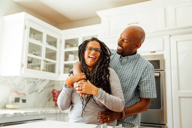 smiling man embracing female partner in kitchen at home - couple  stock pictures, royalty-free photos & images