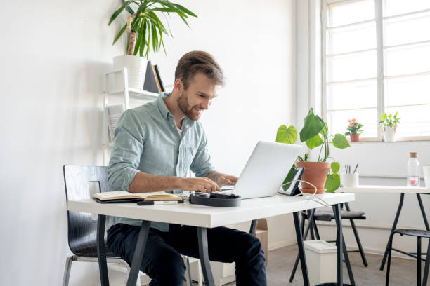 smiling man using laptop at desk in office - web designer stock pictures, royalty-free photos & images