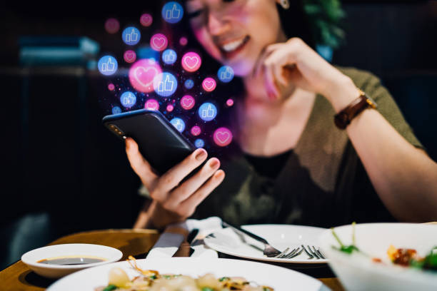 smiling young asian woman using smartphone on social media network application while having meal in the restaurant, viewing or giving likes, love, comment, friends and pages. social media addiction concept - marketing  - fotografias e filmes do acervo