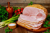 Smoked boneless ham with vegetables and salt on wooden table.