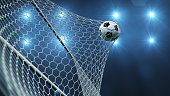 Soccer ball flew into the goal. Soccer ball bends the net, against the background of flashes of light. Soccer ball in goal net on blue background. A moment of delight. 3D illustration