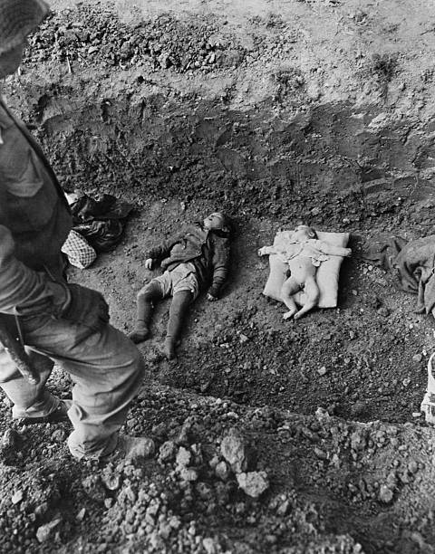 A soldier stands over a baby and a child lying dead in a shallow grave They were murdered at a Nazi concentration camp