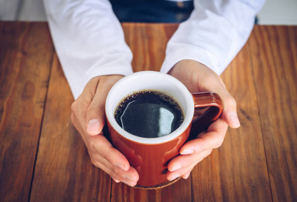 someone hands holding a mug of black coffee before drinking. - coffee stock pictures, royalty-free photos & images