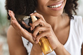 Split Ends Treatment. Smiling Black Woman Spraying Essential Oil On Curly Hair