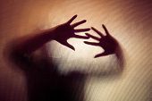 Spooky silhouette of woman with hands pressed against glass window