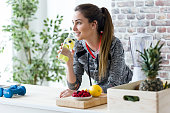Sporty young woman looking sideways while drinking lemon juice in the kitchen at home.